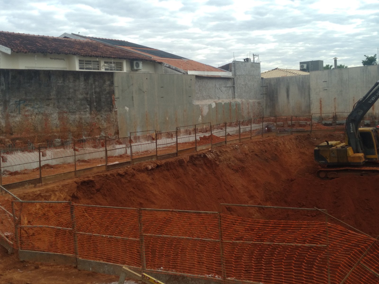 Escavação em andamento com retroescavadeira e muro de contenção